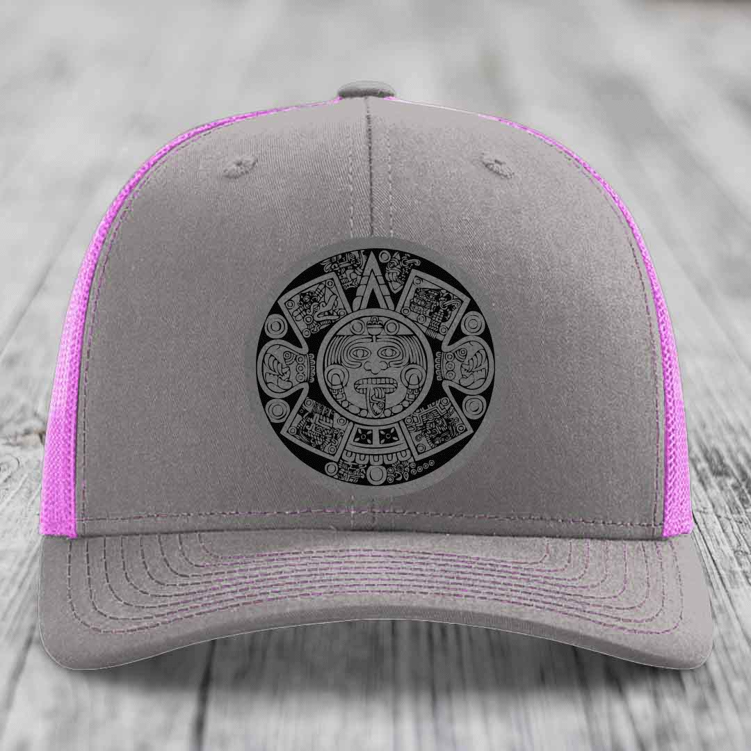 Grey trucker hat with pink mesh sides and a black Aztec calendar patch on the front.