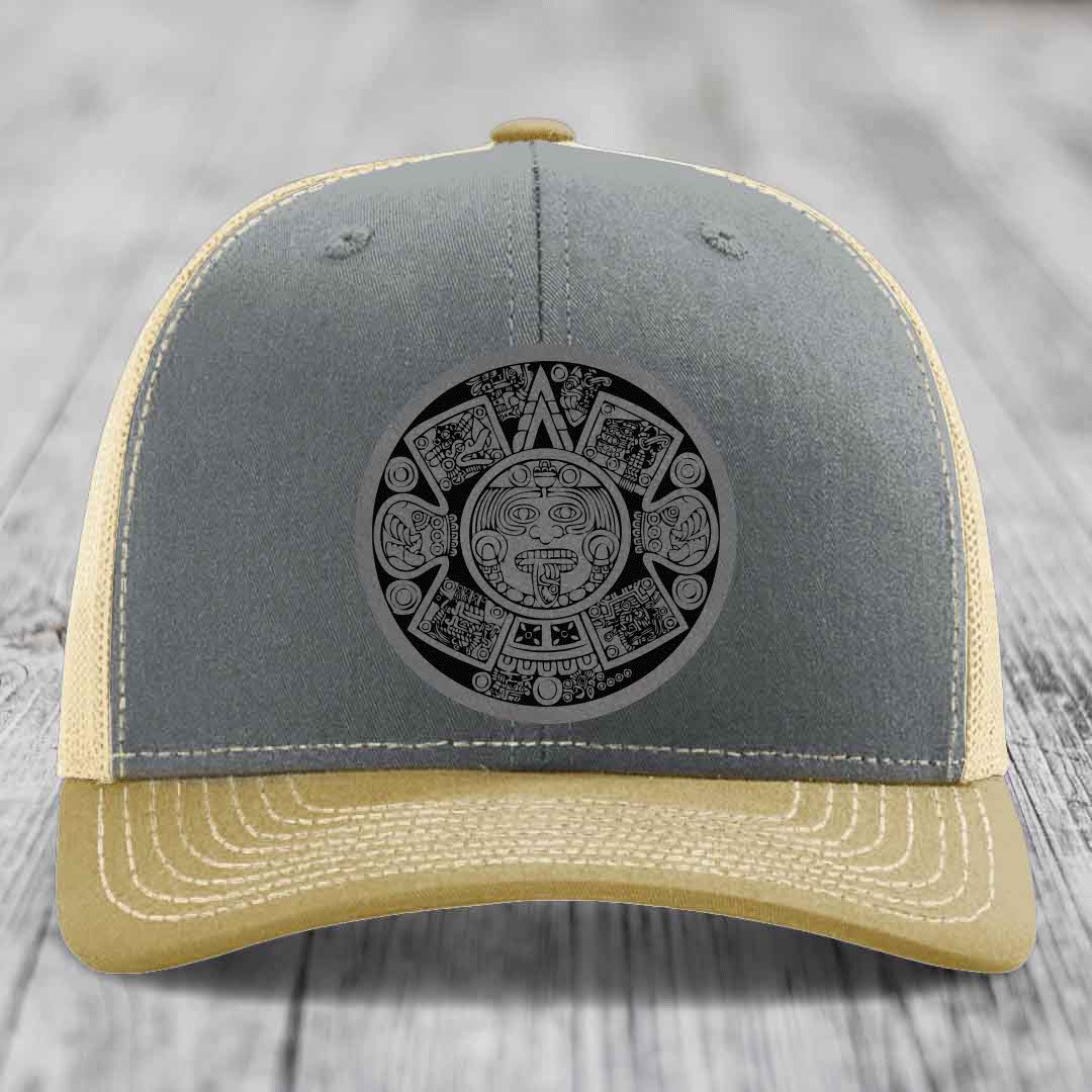 Grey and beige trucker hat with Aztec calendar leather patch on front.
