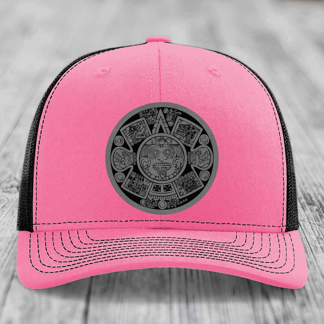 Pink trucker hat with black mesh back and gray Aztec calendar patch on front.