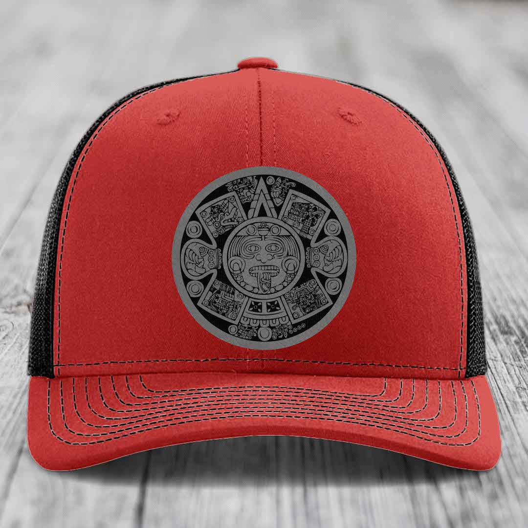 Red trucker hat with black mesh back and gray Aztec calendar patch on front.
