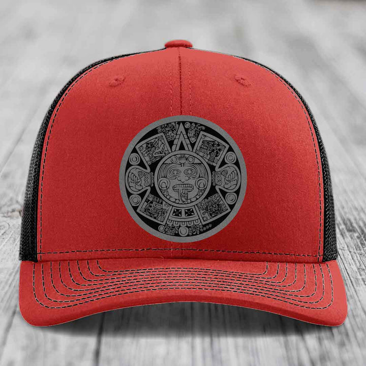 Red trucker hat with black mesh back and gray Aztec calendar patch on front.