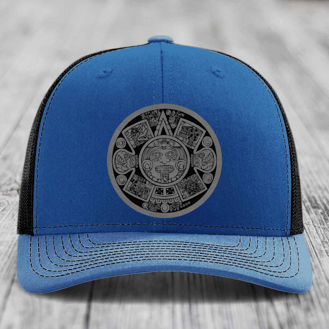 Blue trucker hat with black mesh back and gray Aztec calendar patch on front.