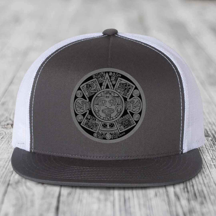 Grey and white trucker hat with Aztec calendar patch on front.