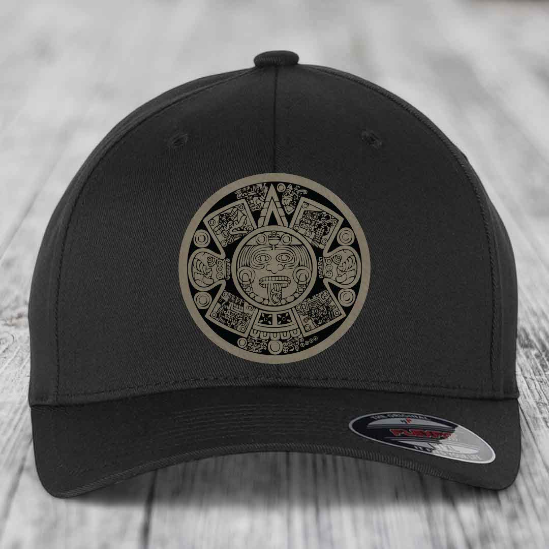 Black baseball cap with Aztec calendar patch on front, sitting on wooden surface.