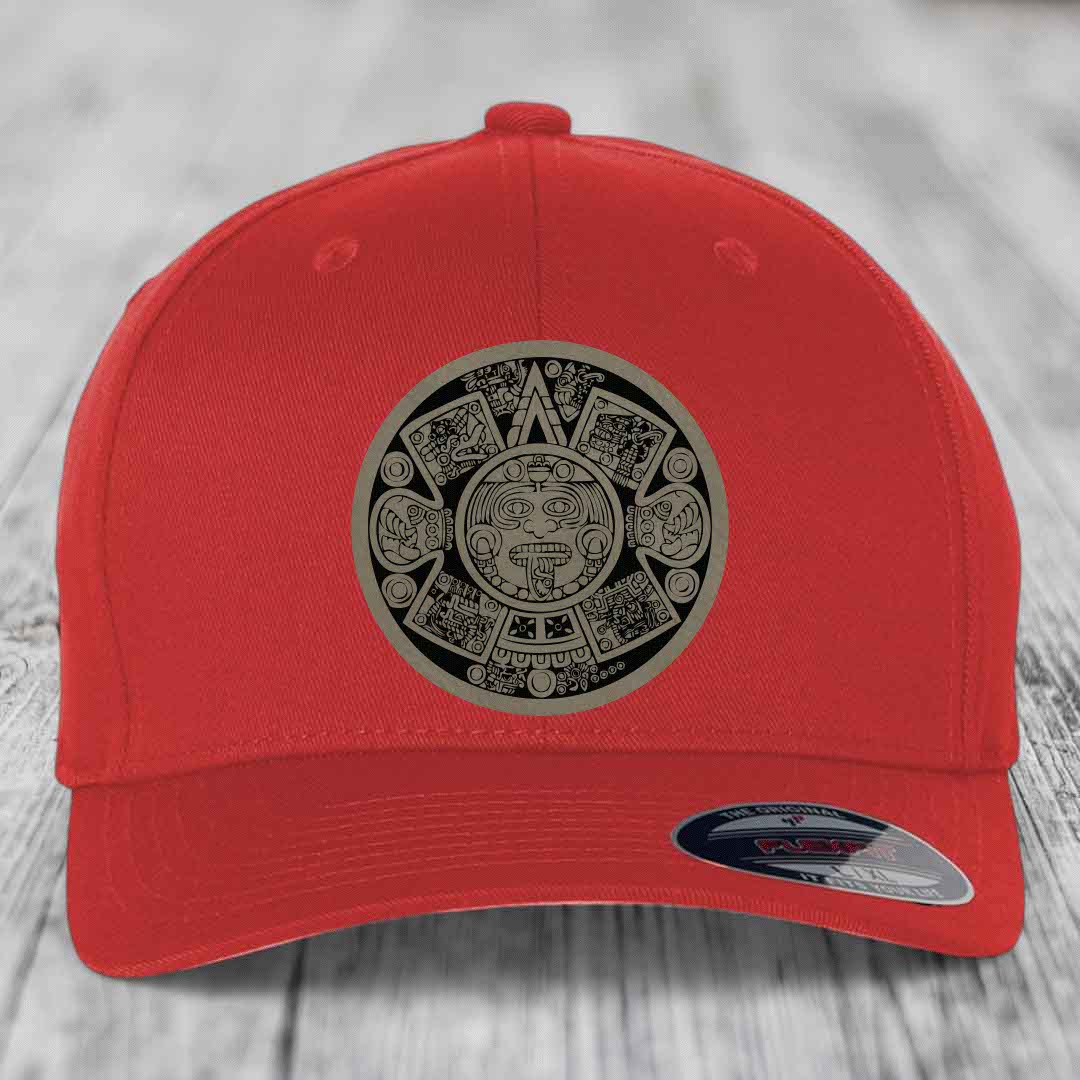 Red baseball cap with Aztec calendar patch on front, displayed on wooden surface.
