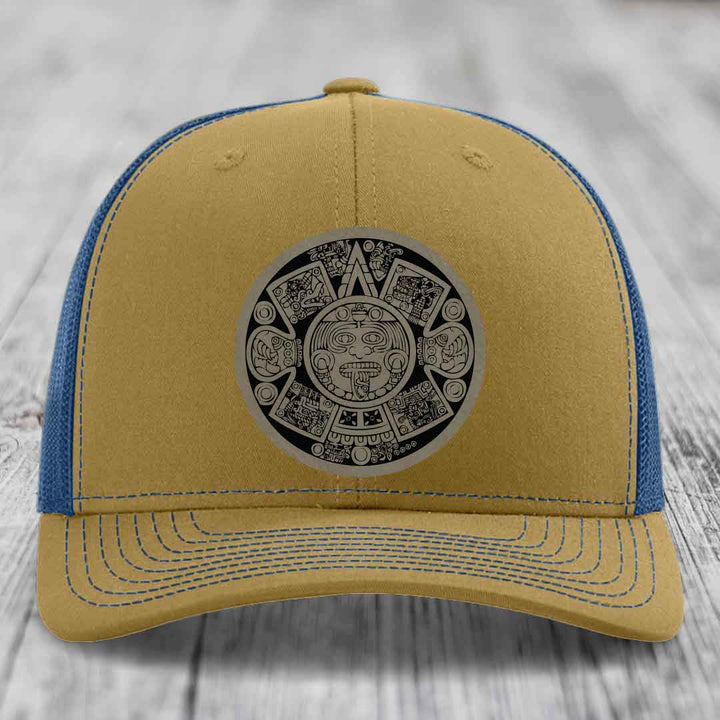 Tan and blue trucker hat with Aztec calendar patch on front.