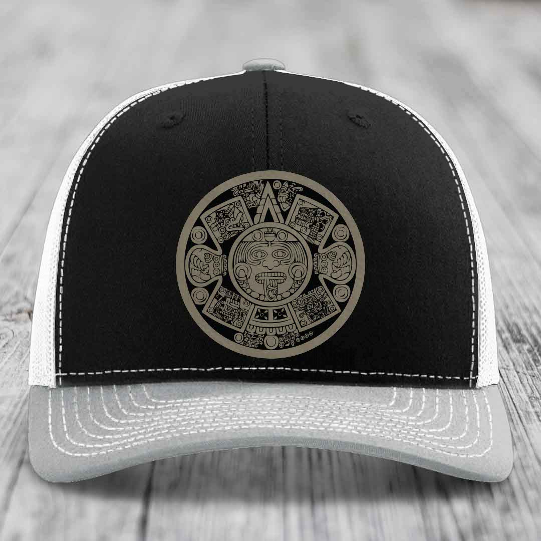 Black and grey trucker hat with Aztec calendar patch on front.