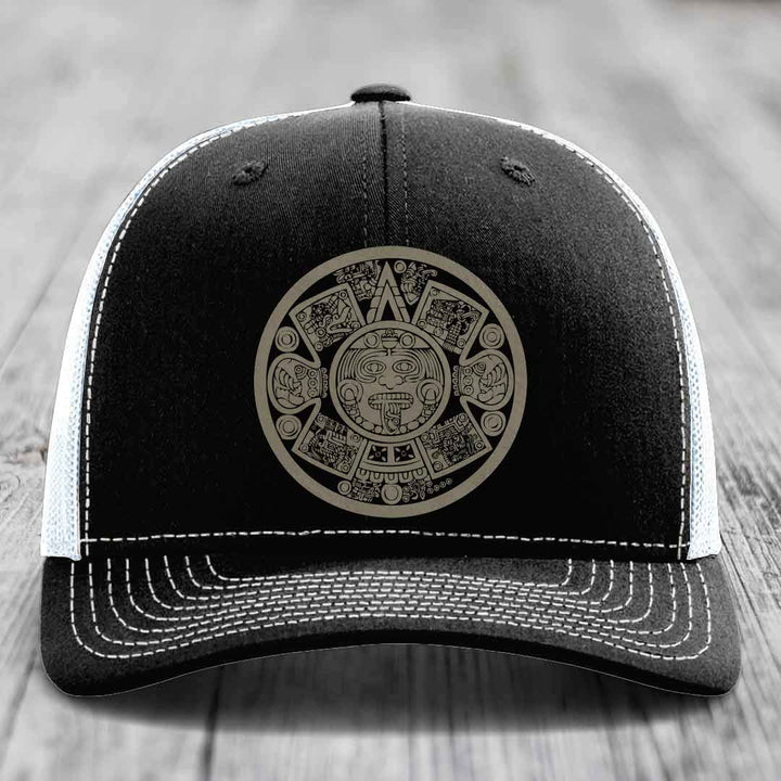 Black trucker hat with white stitching and an Aztec calendar patch on the front.