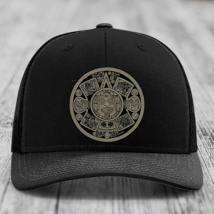 Black trucker hat with Aztec calendar design patch on front.