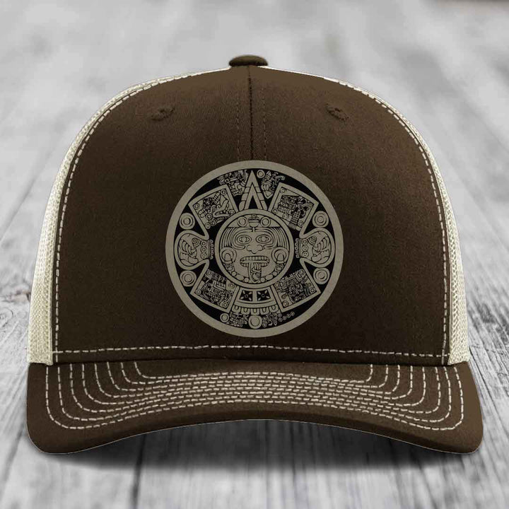 Brown trucker hat with white stitching and an Aztec calendar patch on the front.