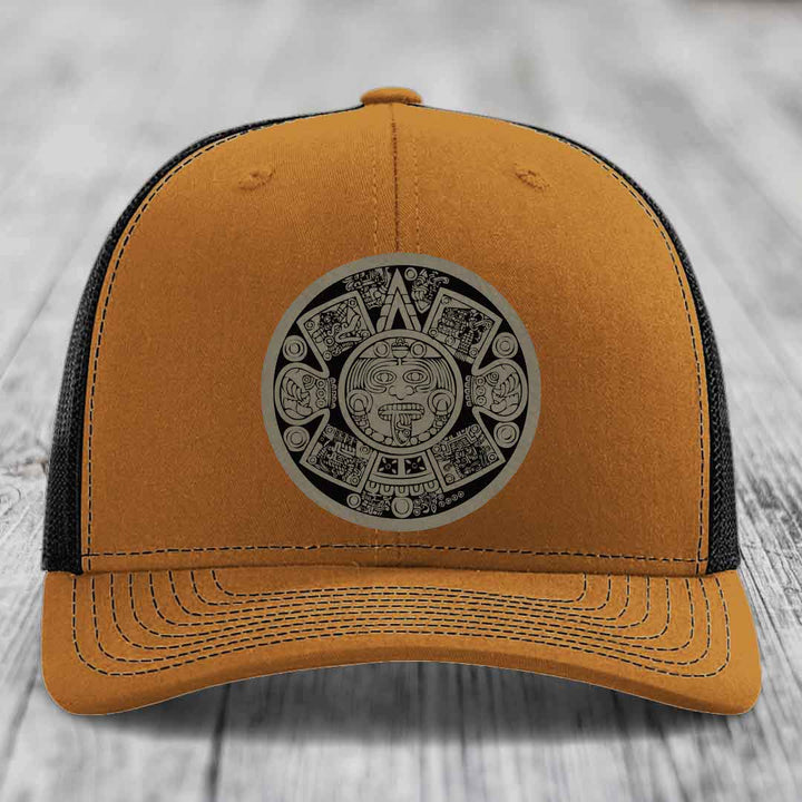 Orange trucker hat with black mesh back and Aztec calendar patch on front.