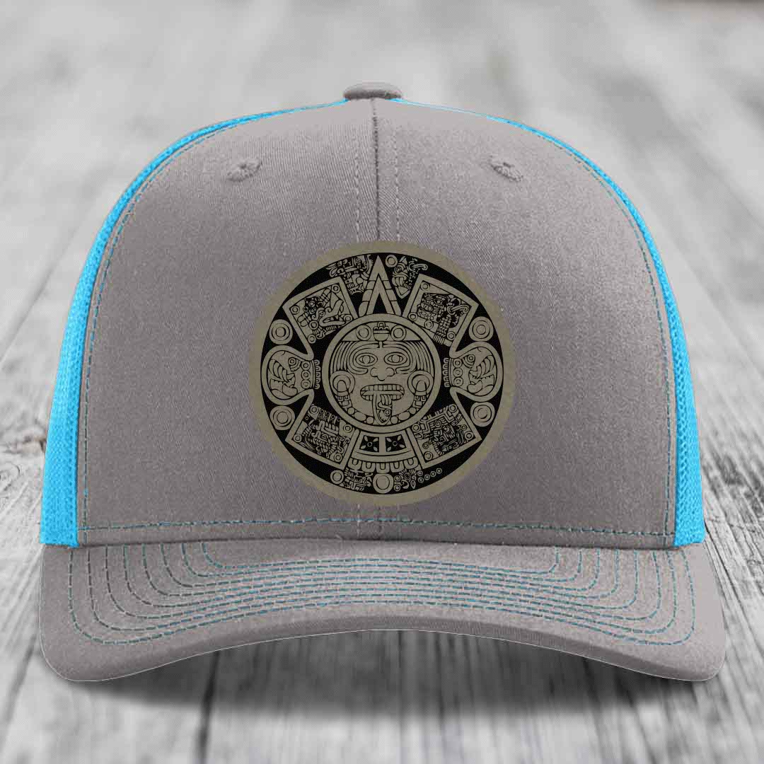 Grey trucker hat with blue mesh sides and a black Aztec calendar leather patch on front.
