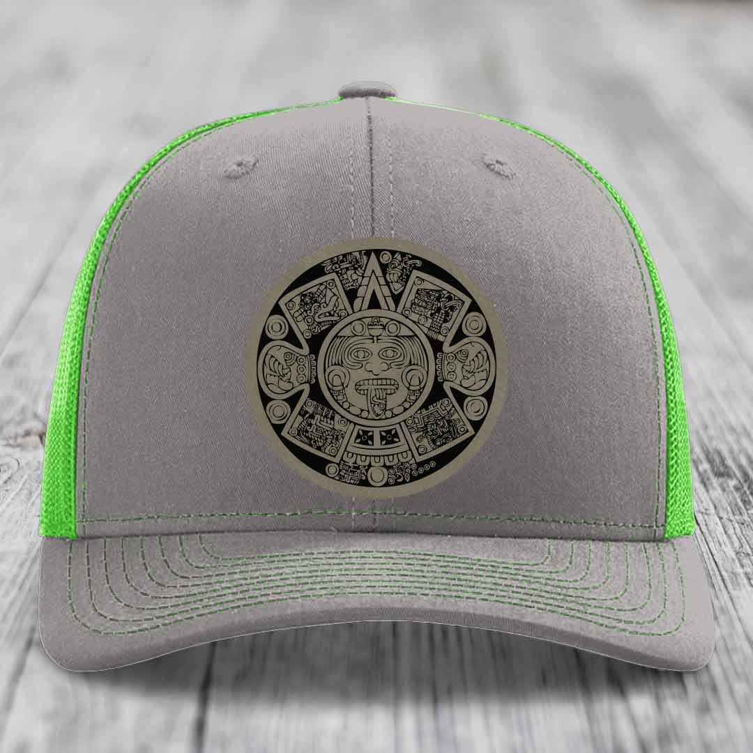 Grey trucker hat with neon green mesh and stitching, featuring an Aztec calendar patch on front.