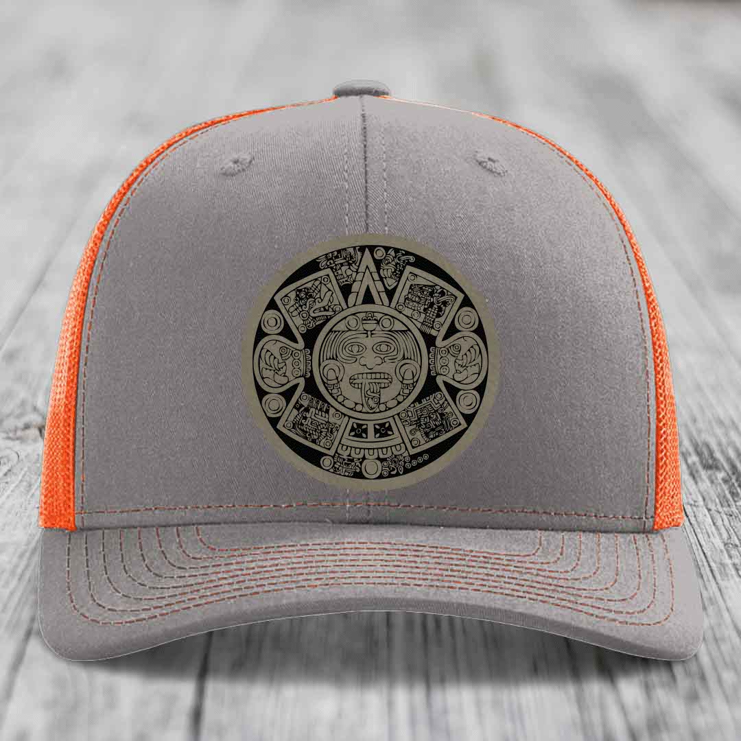 Grey trucker hat with orange mesh back and Aztec calendar patch on front.