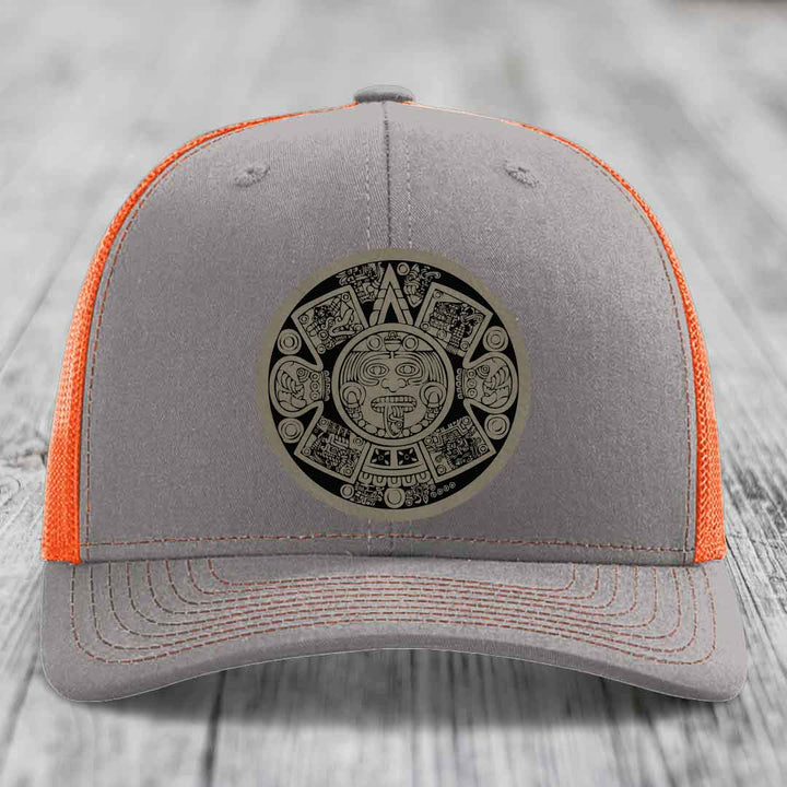 Grey trucker hat with orange mesh back and Aztec calendar patch on front.