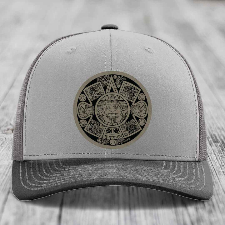 Grey trucker hat with Aztec calendar leather patch on front.