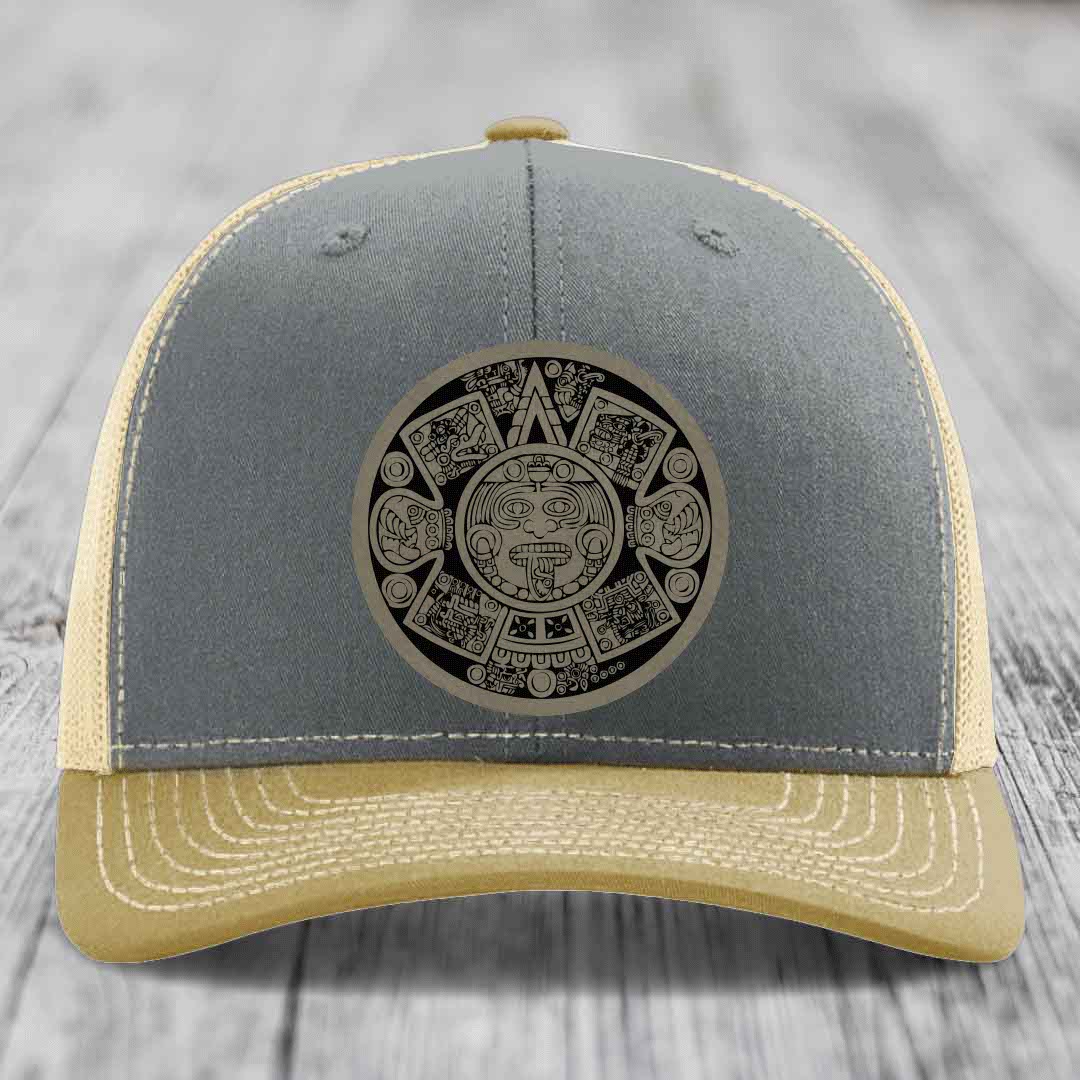 Grey and beige trucker hat with Aztec calendar patch on front.