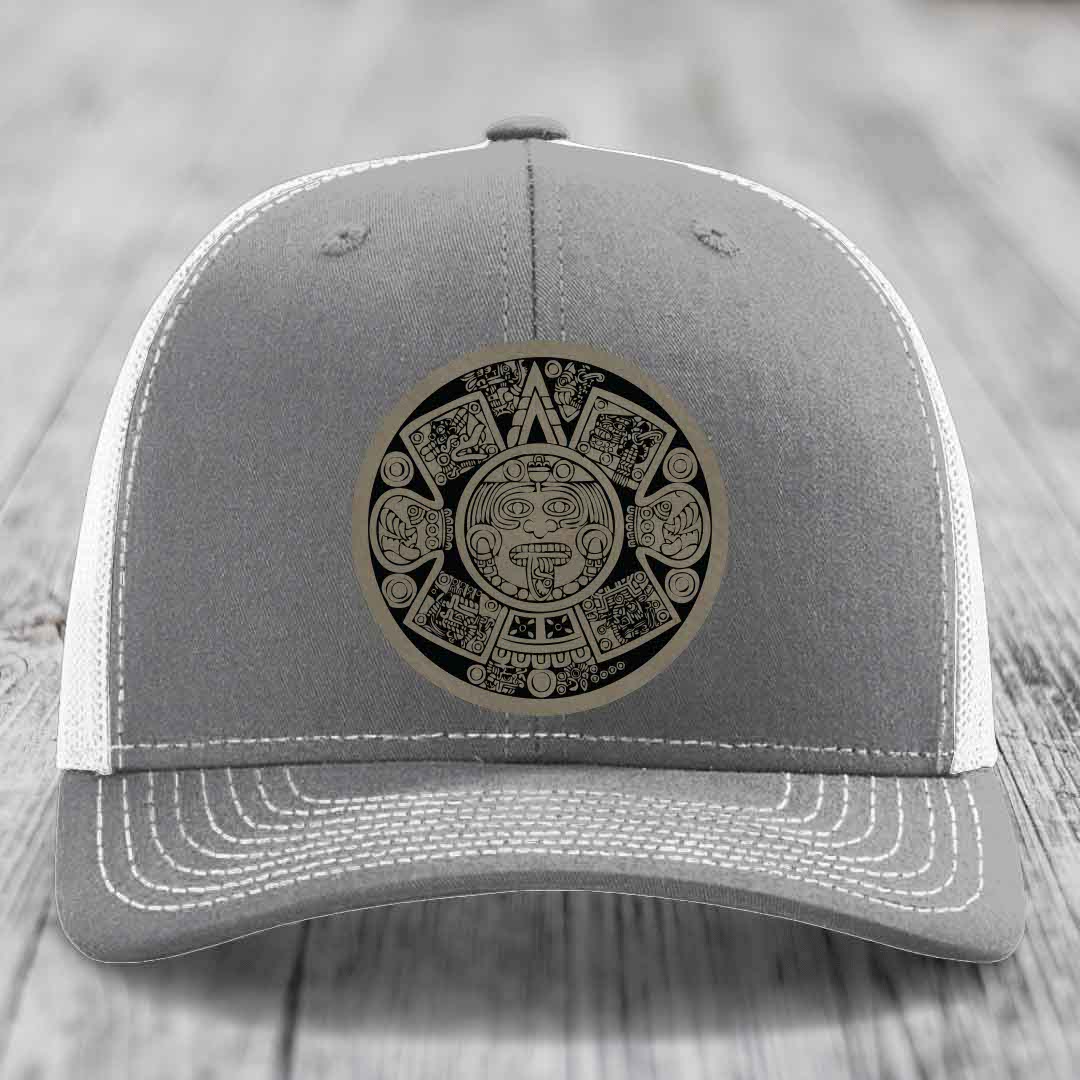 Grey trucker hat with white mesh back and stitching, featuring a circular Aztec calendar leather patch.
