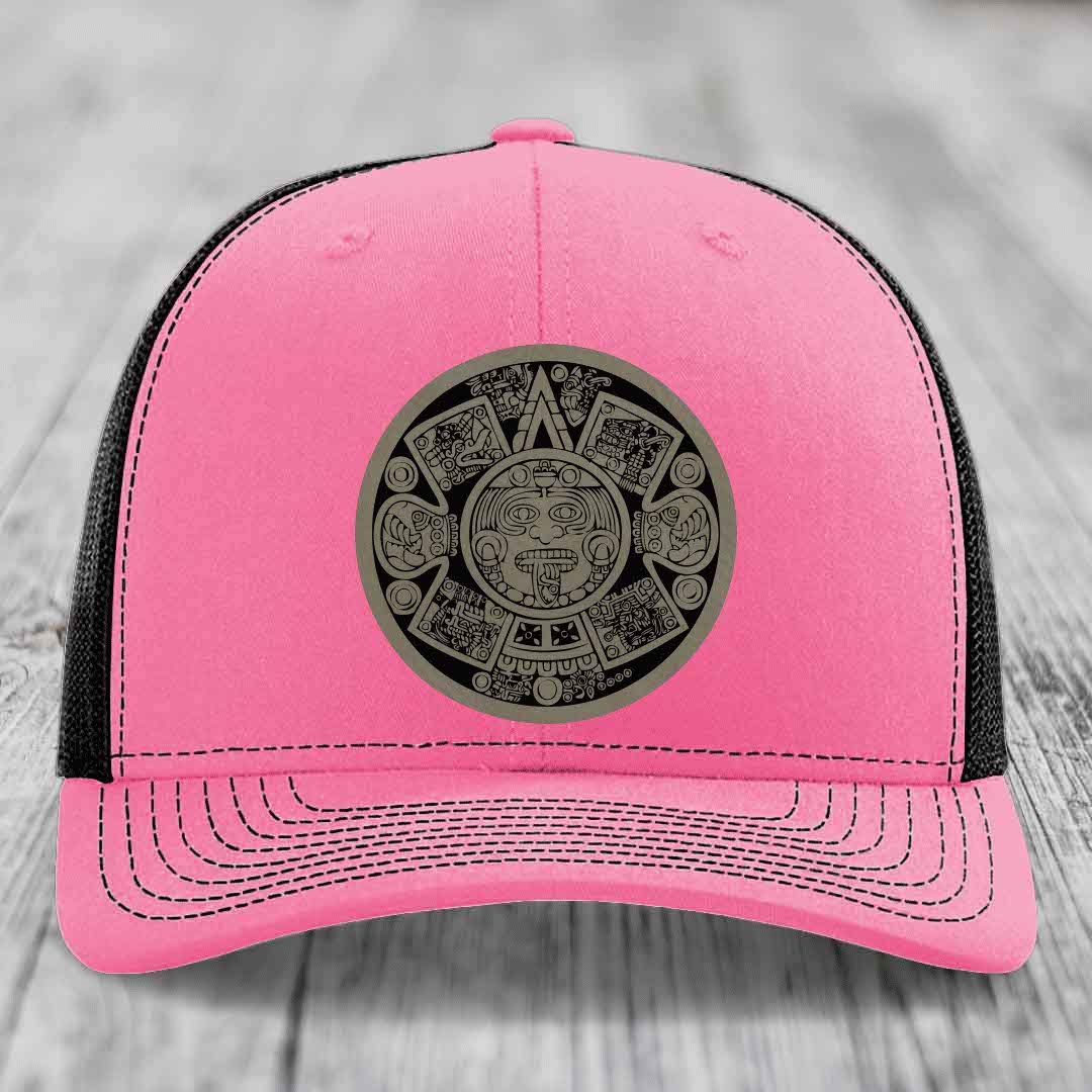 Pink trucker hat with black mesh back and gray Aztec calendar patch on front.