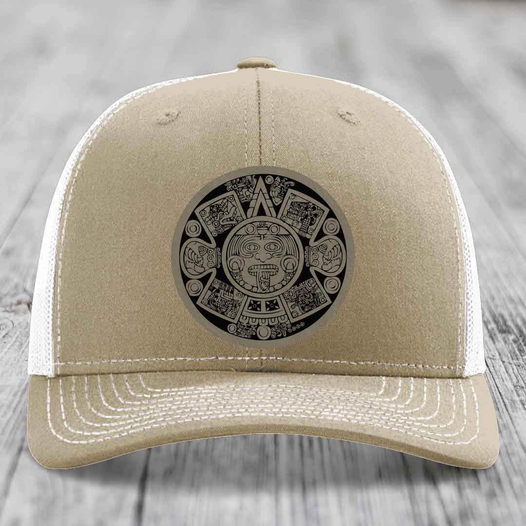 Beige trucker hat with white mesh back and embroidered Aztec calendar patch on front.