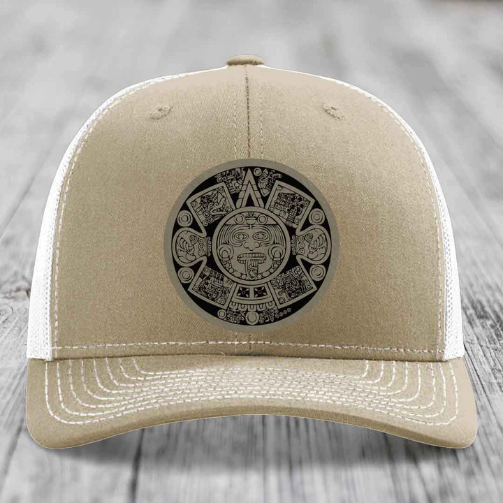 Beige trucker hat with white mesh back and embroidered Aztec calendar patch on front.