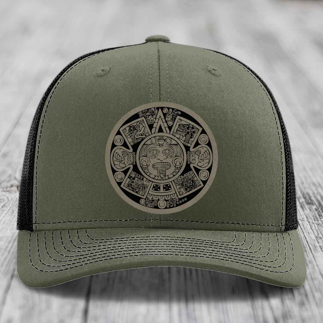 Olive green trucker hat with Aztec calendar patch on front, black mesh back.