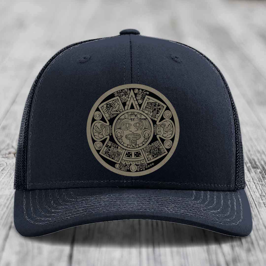 Black trucker hat with Aztec calendar design patch on front, placed on wooden surface.