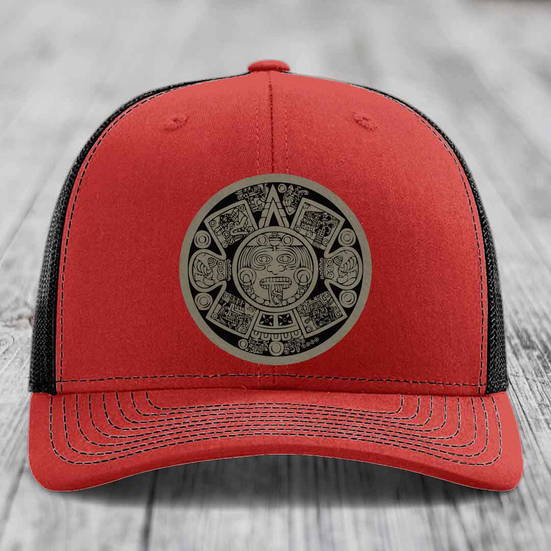 Red trucker hat with black mesh back and an Aztec calendar patch on front.