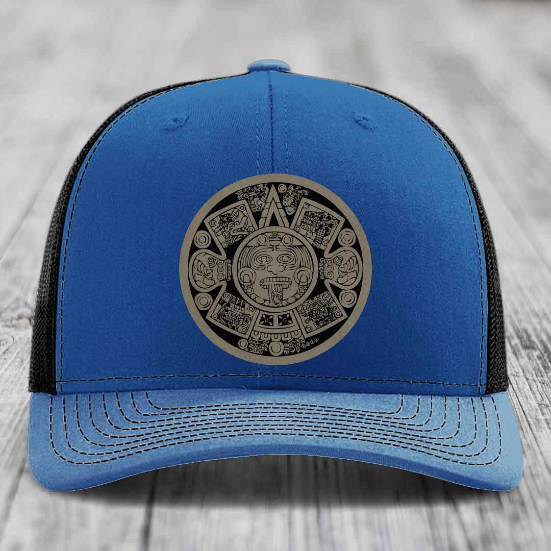 Blue trucker hat with black mesh back and an Aztec calendar patch on the front.