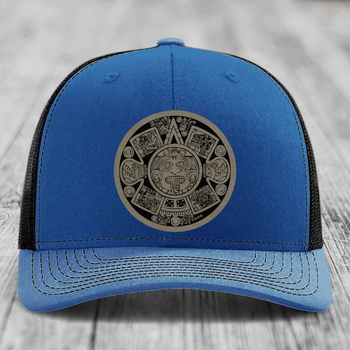 Blue trucker hat with black mesh back and an Aztec calendar patch on the front.