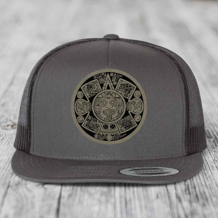 Grey trucker hat with Aztec calendar patch on front, flat brim, mesh back.