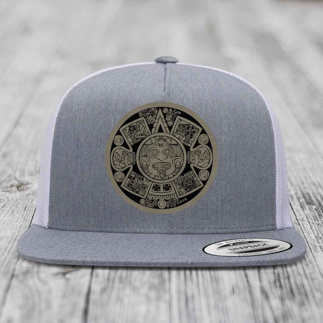 Grey trucker hat with Aztec calendar patch on front, white mesh back, flat brim.
