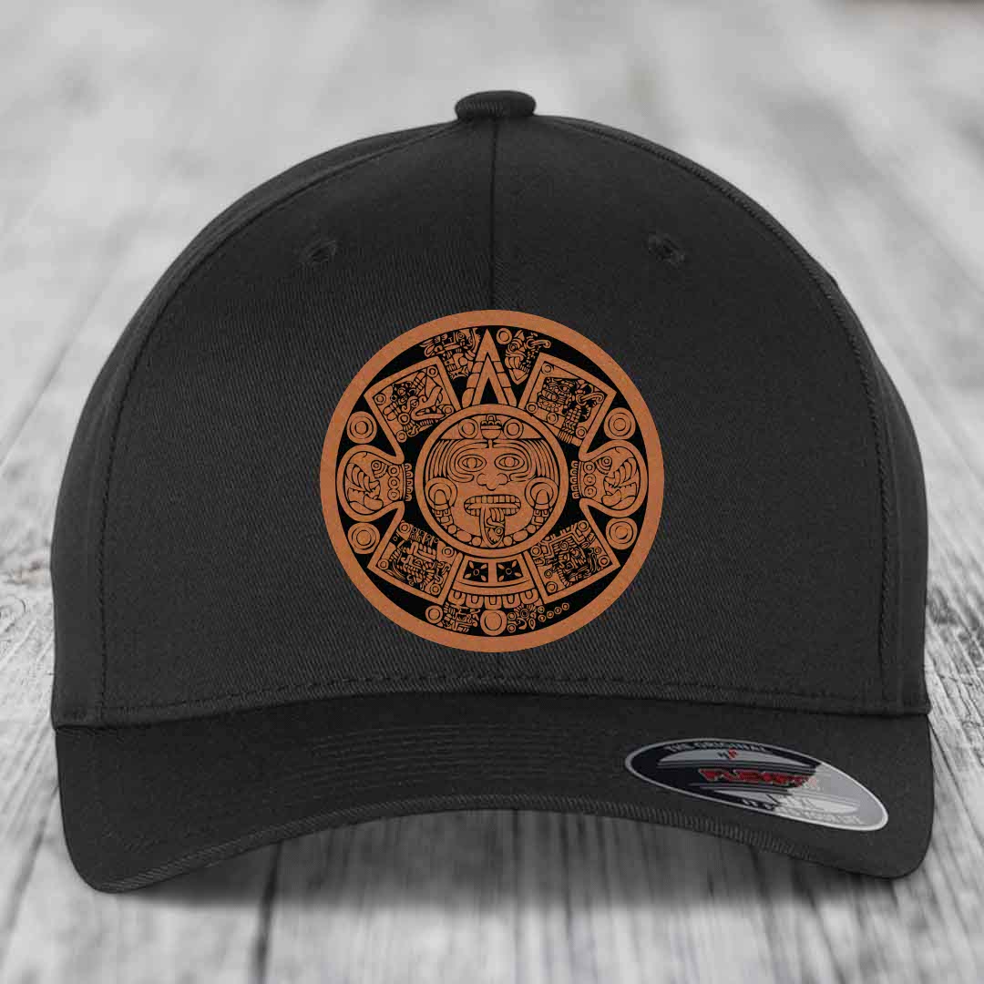 Black baseball cap with brown Aztec calendar patch on front, displayed on wooden surface.