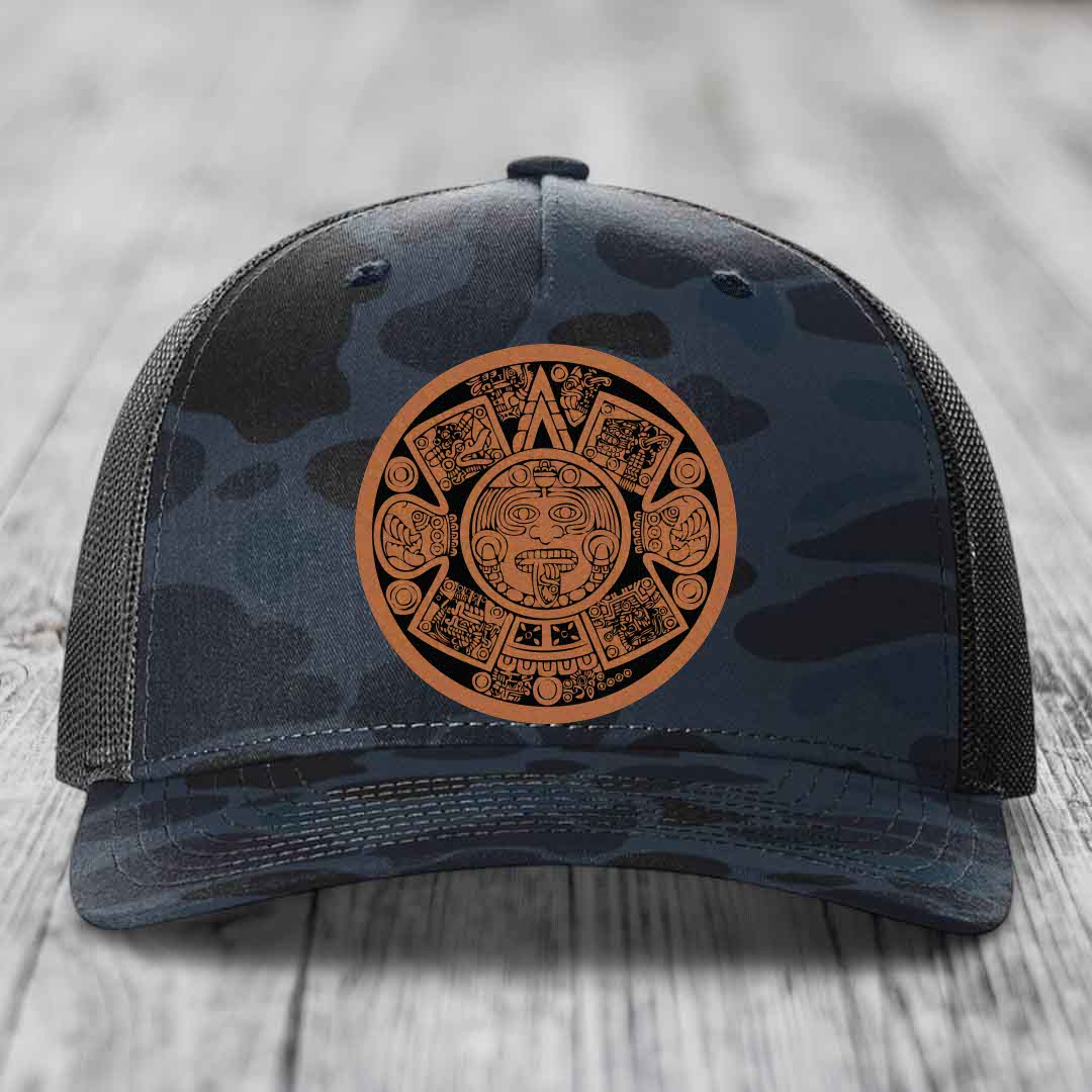 Camouflage trucker hat with brown Aztec calendar patch on front.