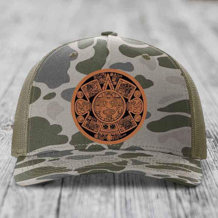 Camouflage trucker hat with brown Aztec calendar leather patch on front.