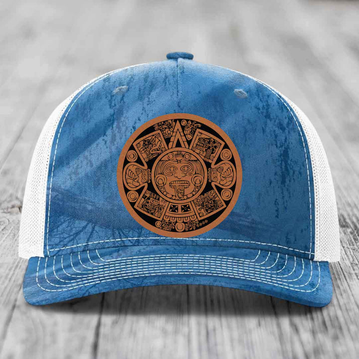 Blue and white trucker hat with a brown Aztec calendar leather patch on the front.