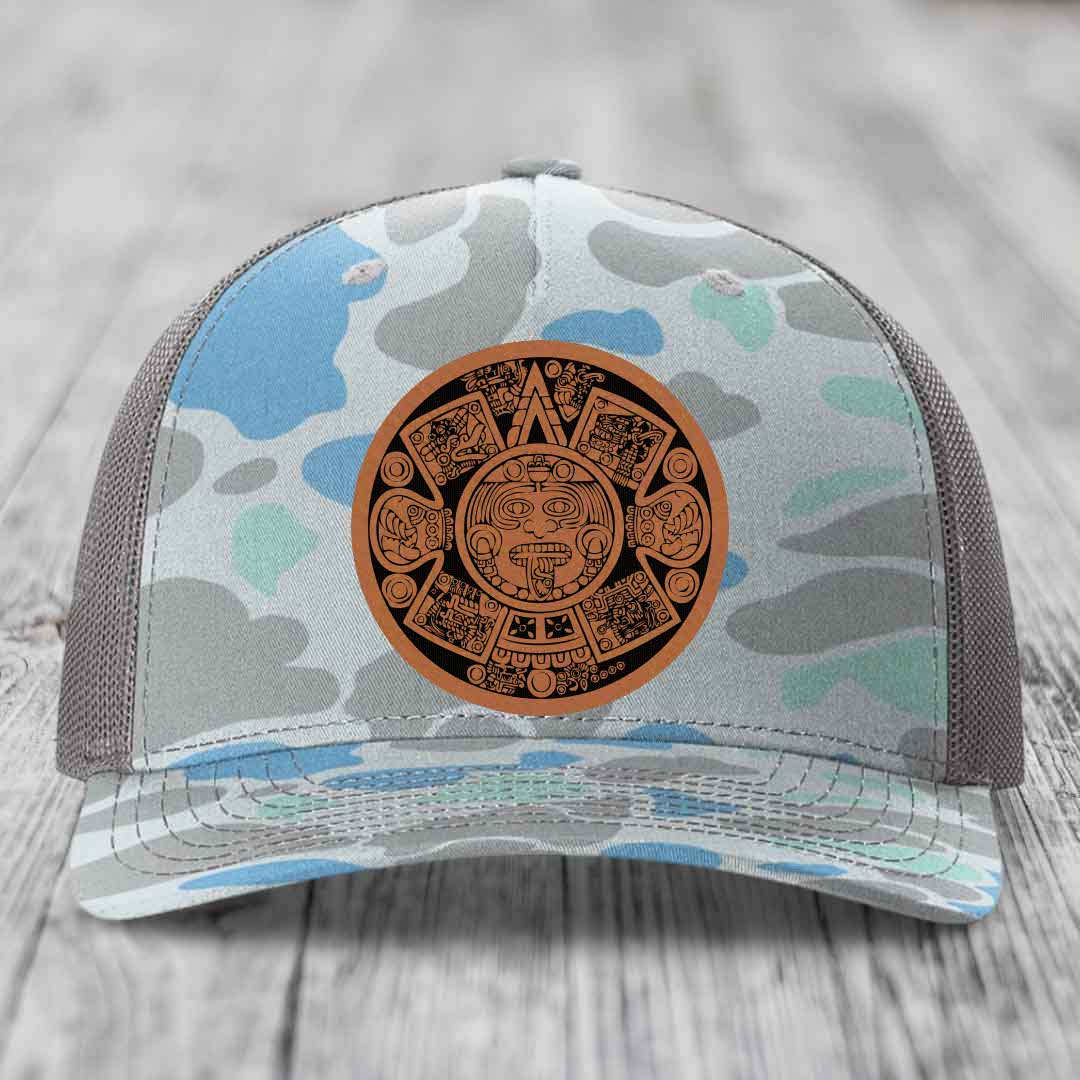 Camouflage trucker hat with brown Aztec calendar leather patch on front.