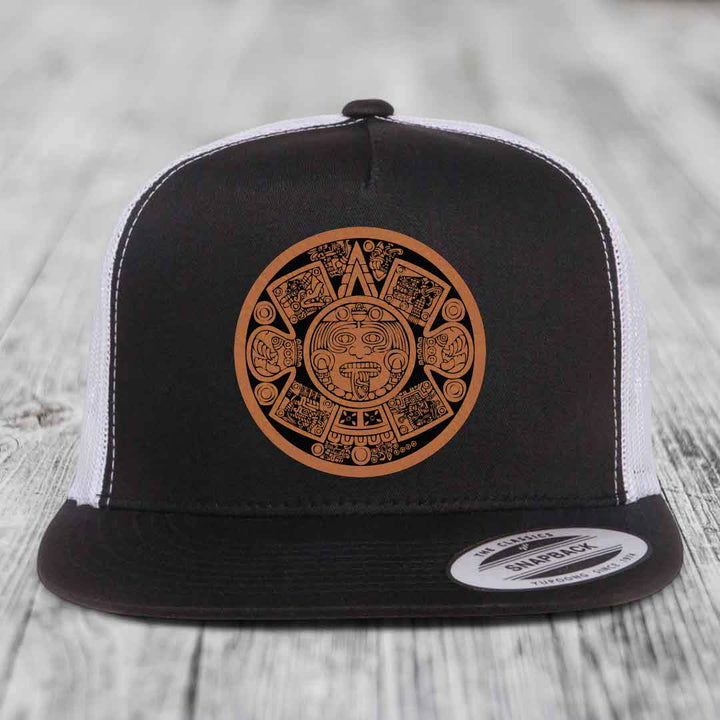 Black and white trucker hat with brown Aztec calendar leather patch on front.