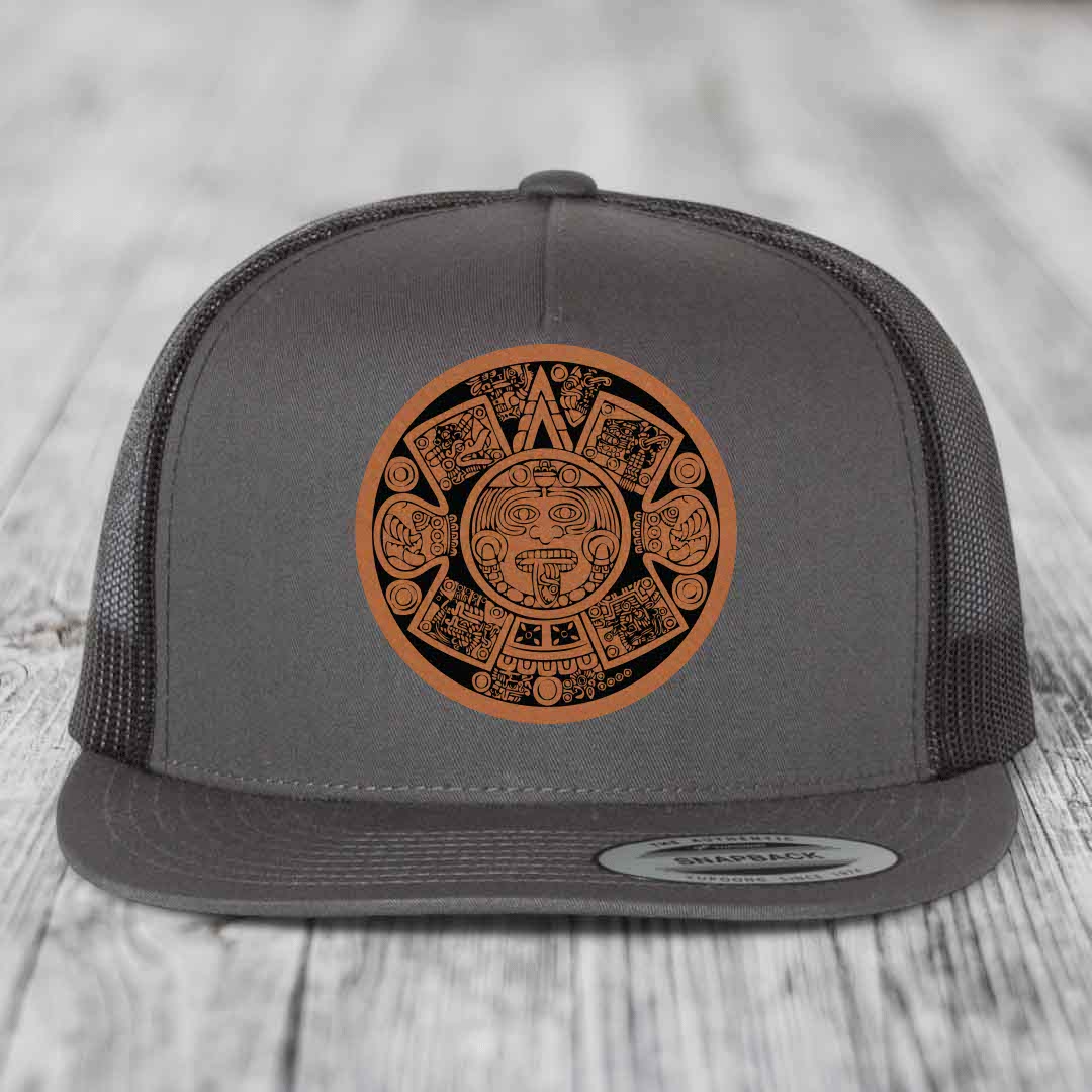 Grey trucker hat with brown Aztec calendar leather patch on front.