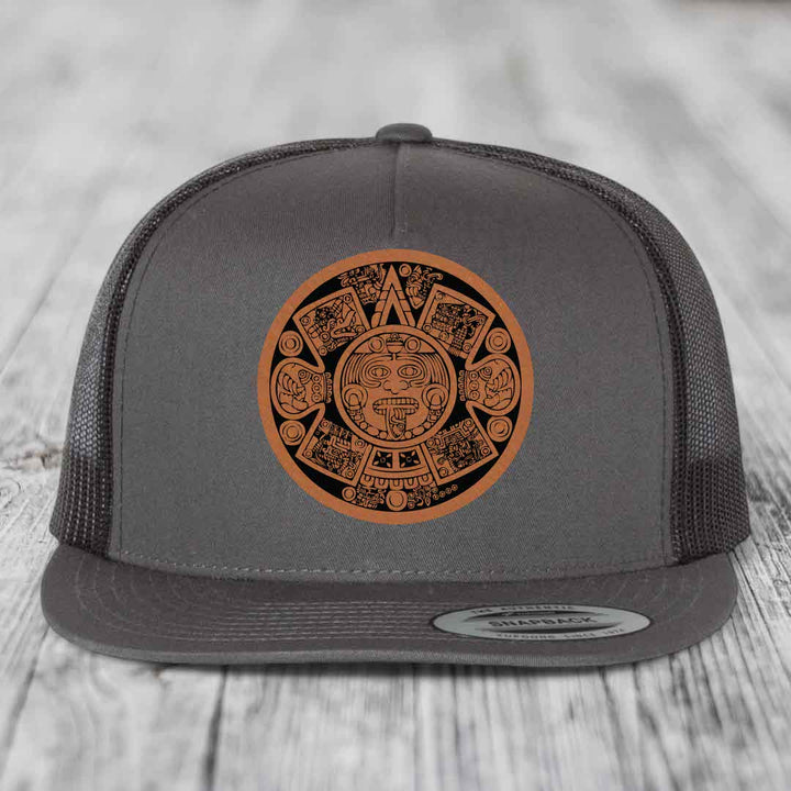 Grey trucker hat with brown Aztec calendar leather patch on front.