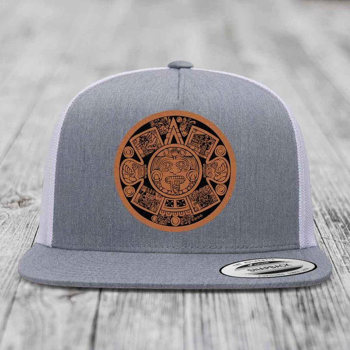 Grey trucker hat with brown Aztec calendar leather patch on front.