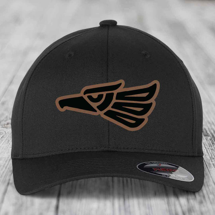 Black baseball cap with Aztec-style eagle patch in black and brown, featuring a Flexfit label.