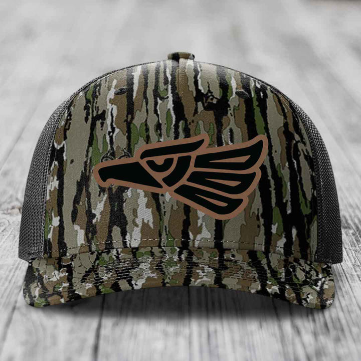 Camouflage trucker hat with black and brown eagle patch on front.