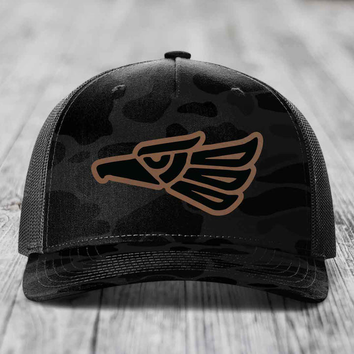Black camouflage trucker hat with brown Aztec eagle patch on front.