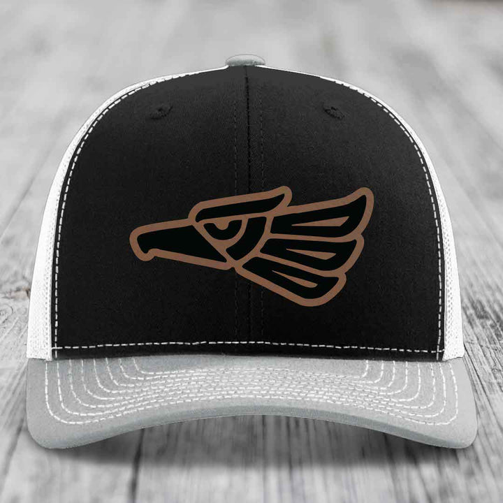 Black and white trucker hat with brown and black Aztec eagle patch on front.