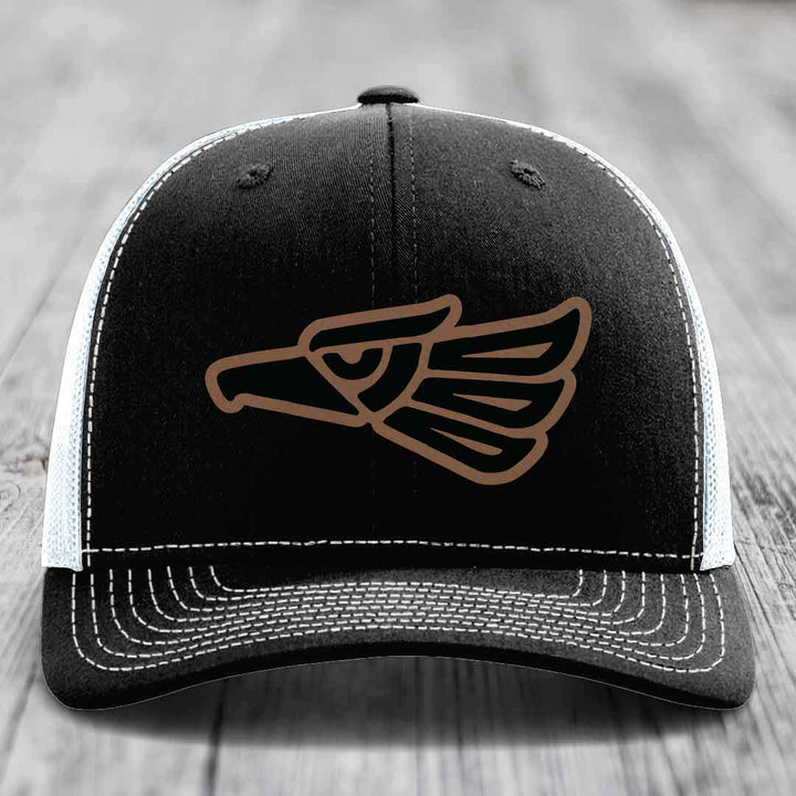 Black trucker hat with brown Aztec eagle patch and white stitching on front panel.