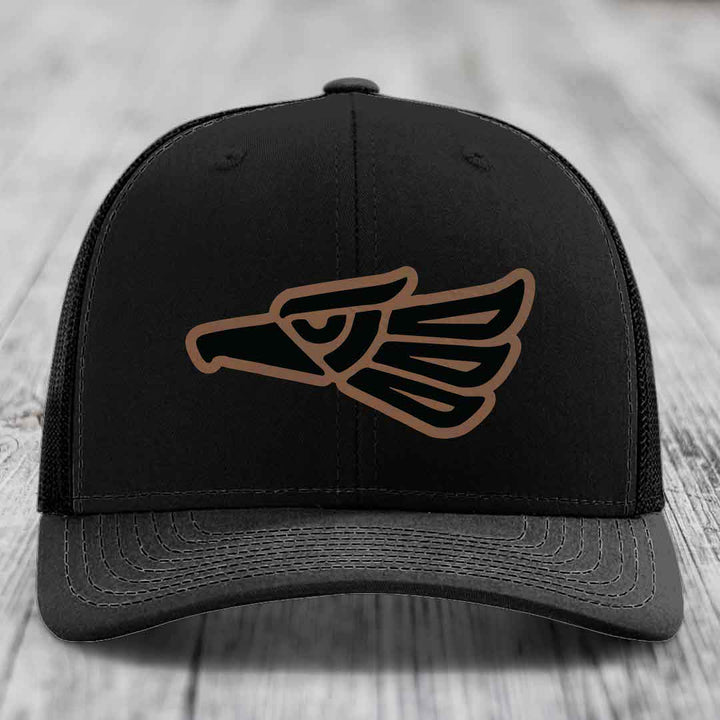 Black trucker hat with brown and black Aztec-style eagle patch on front.