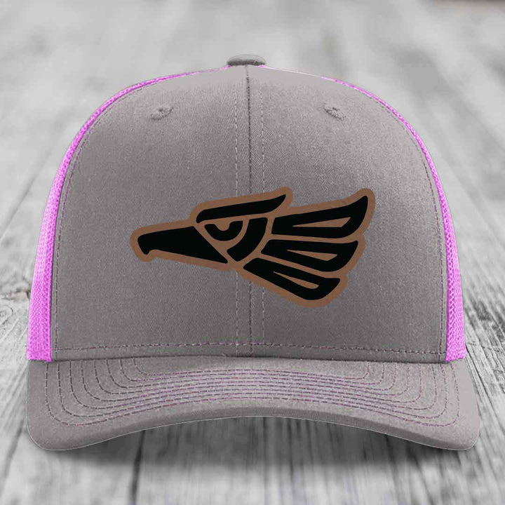 Grey trucker hat with pink mesh sides and a black Aztec-style eagle patch on front.