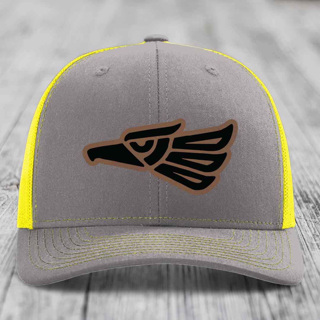 Grey trucker hat with yellow mesh and stitching, featuring a black and brown Aztec-style eagle patch.