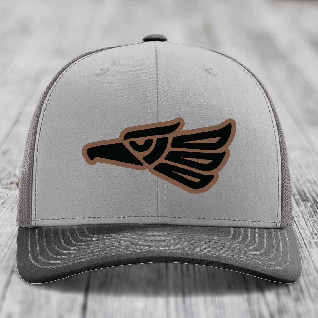 Grey trucker hat with black and brown Aztec eagle leather patch on front.